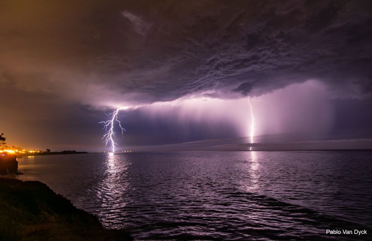 A stormy night along the coast as two lightning bolts strike in the distance.